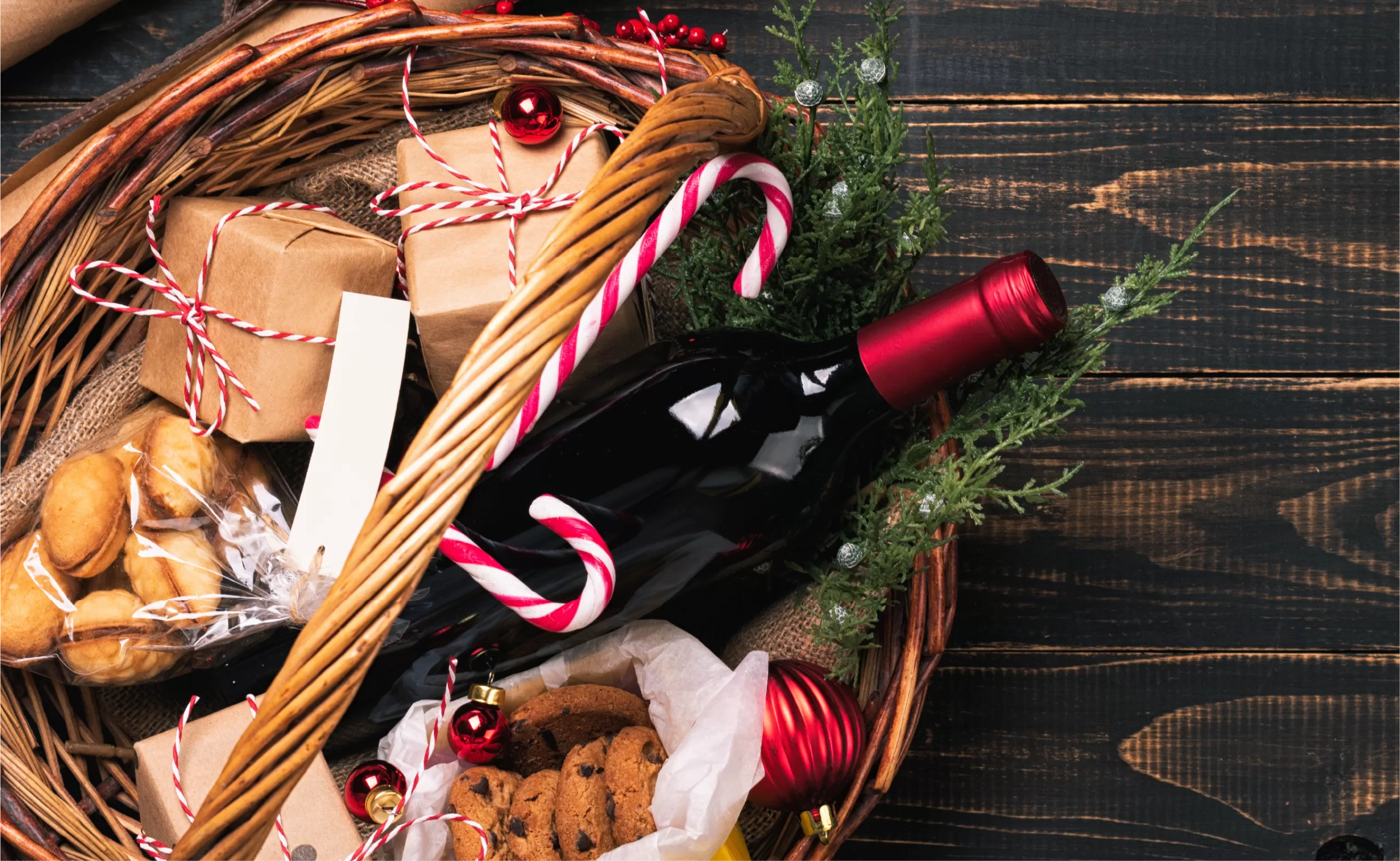 red wine Christmas gift basket with candy canes and cookies on a wooden table