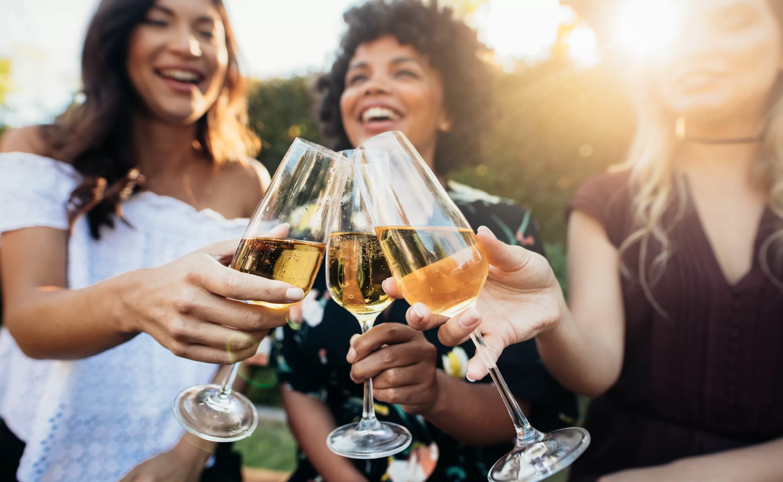 three young women enjoying white wine in a vineyard during golden hour