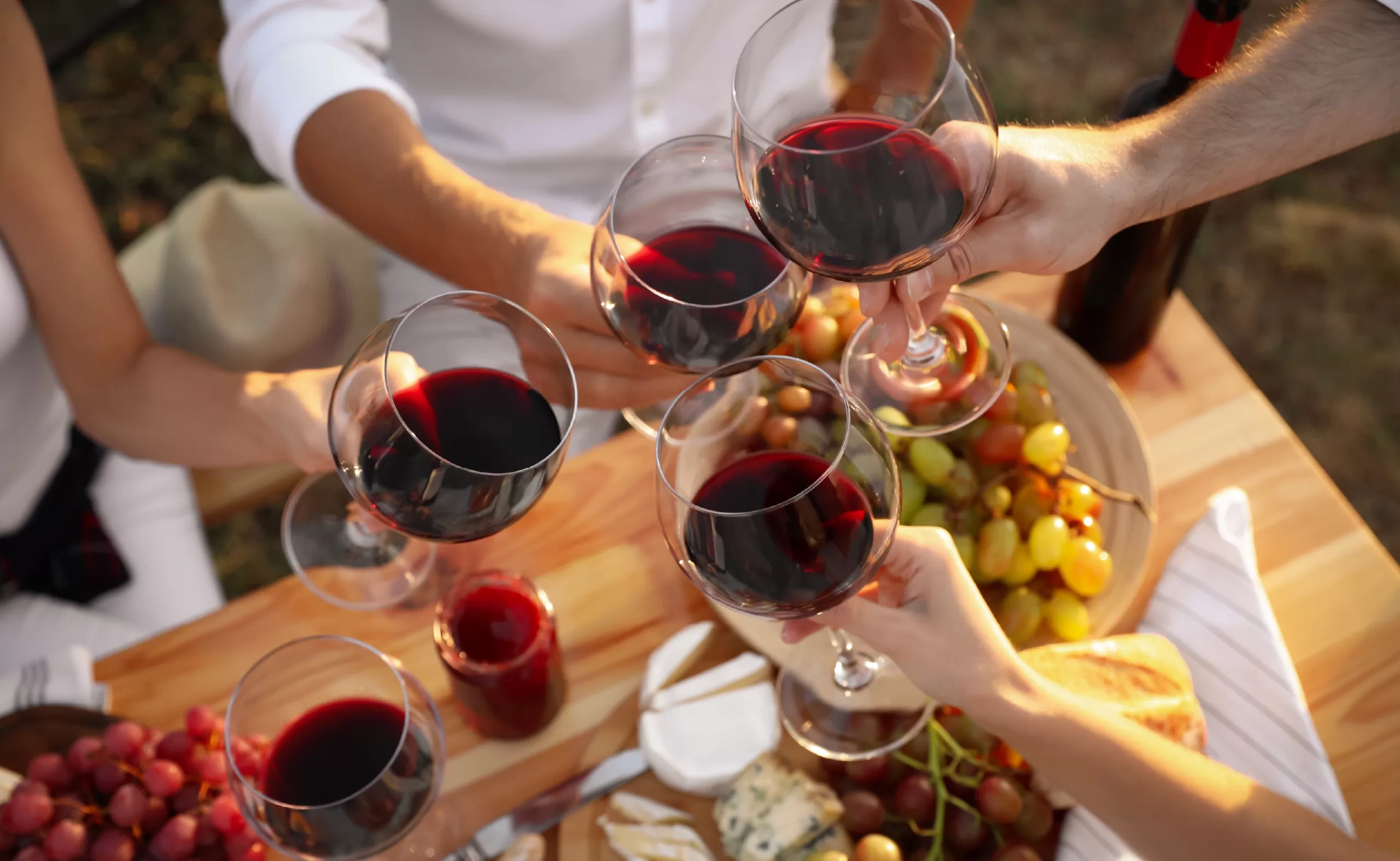 a group of four friends in the hill country clink wine classes filled with red wine over a table spread with cheese, crackers, and grapes during the fall